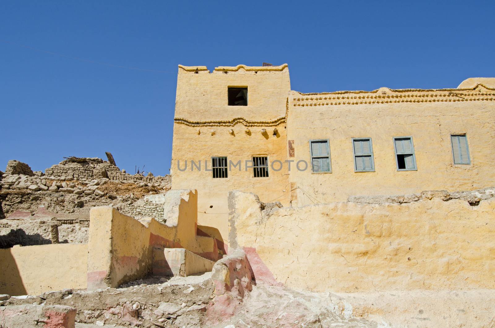 A traditional mud brick home painted yellow with some elegant detail in the village of Qurnet Murai.  The house is one of many built over the top of Ancient Egyptian tombs on the West Bank of the Nile in Luxor, Egypt.