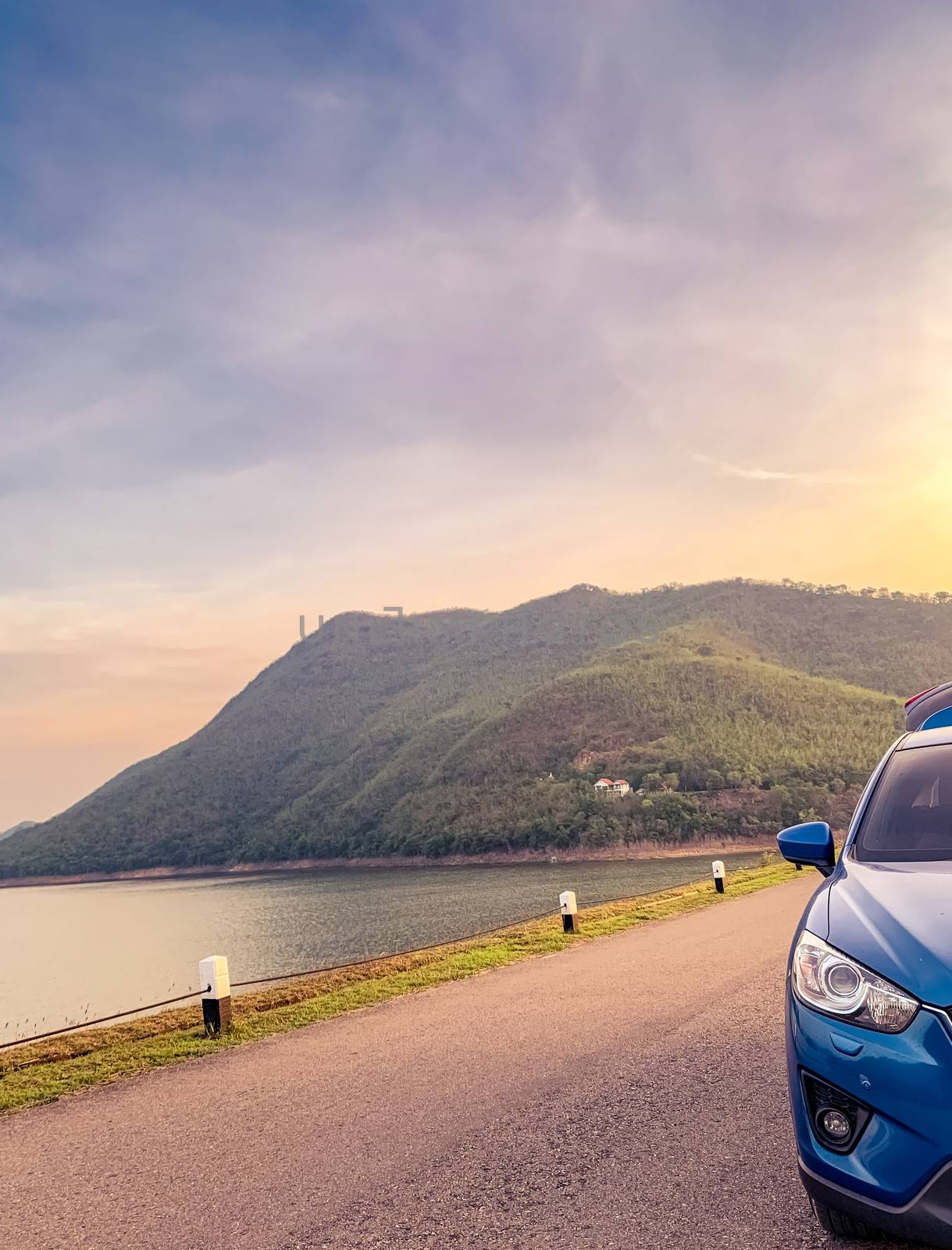 Front view of blue SUV car with opened car truck parked on asphalt road at dam. Summer road trip travel. Car parked on the road in front of the mountain beside reservoir. Summer vacation with nature.