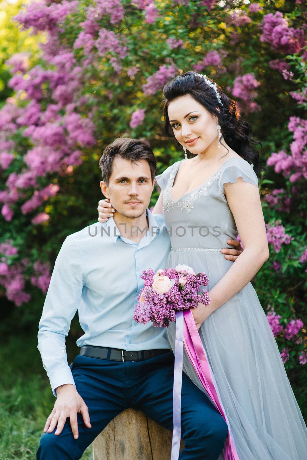 a guy and a girl walk in the spring garden of lilacs before the wedding ceremony