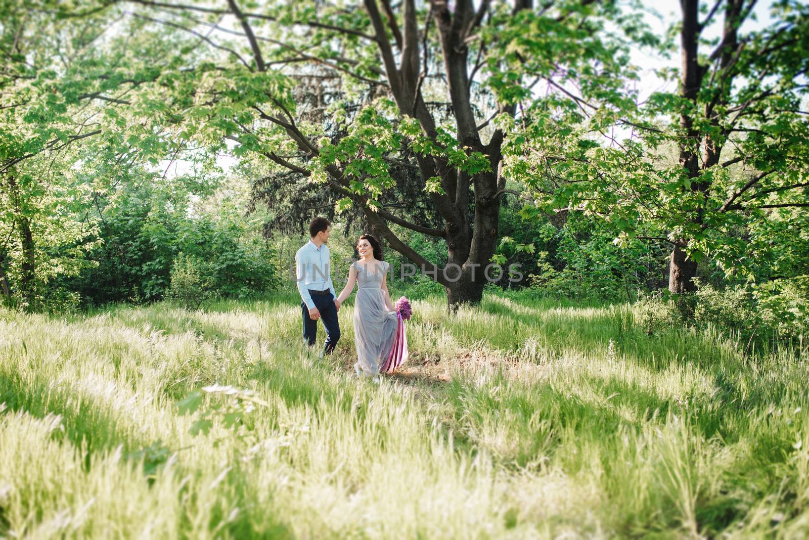 a guy and a girl walk in the spring garden of lilacs before the wedding ceremony