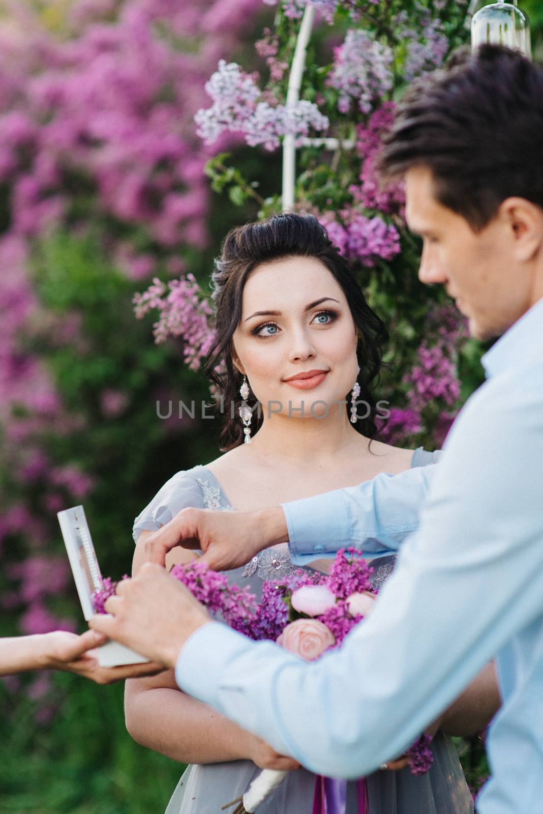 the groom dresses the bride with wedding rings near the lilac arch