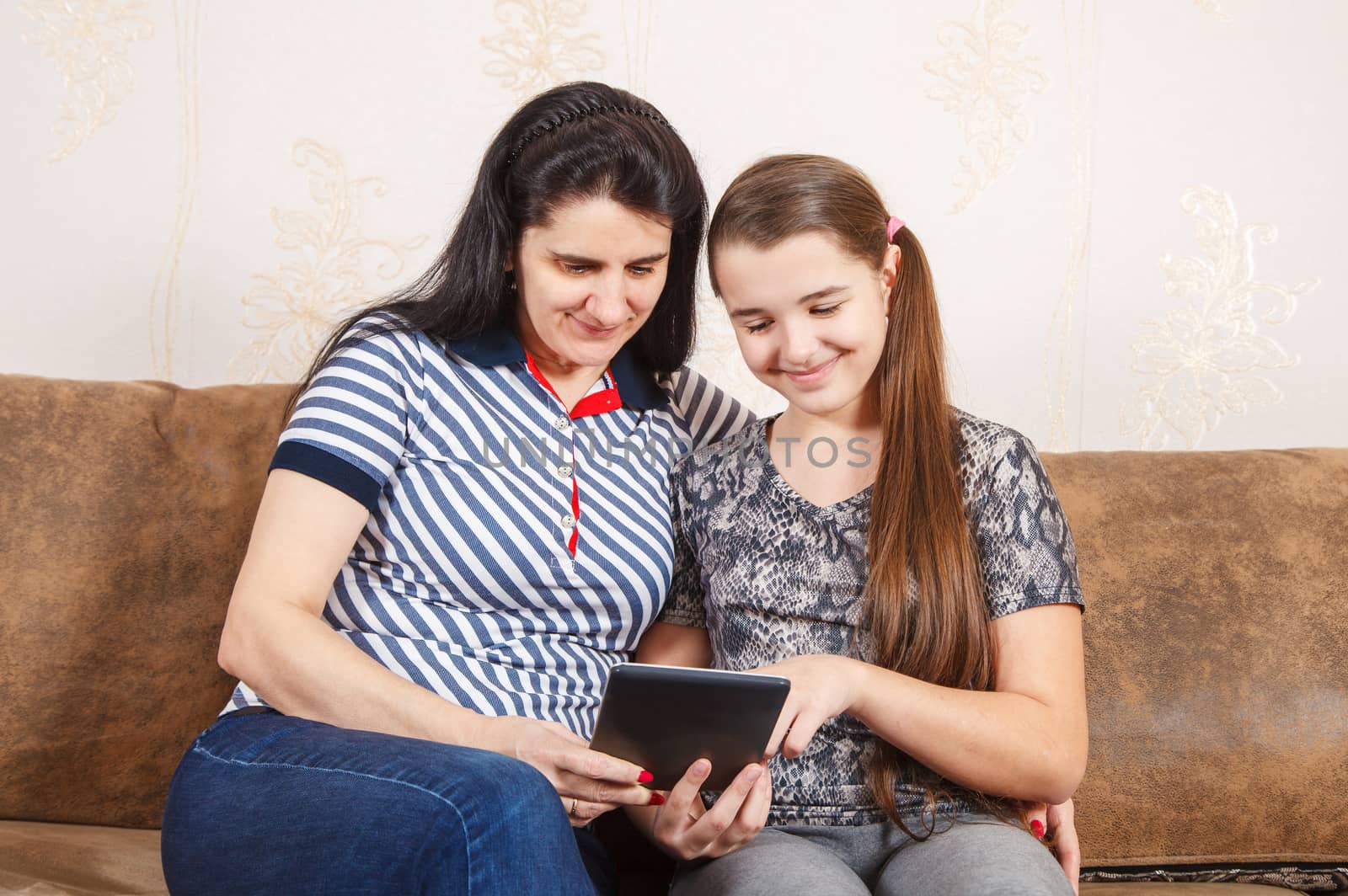 mom and daughter look at the tablet display while sitting on a sofa at home. coronavirus quarantine.