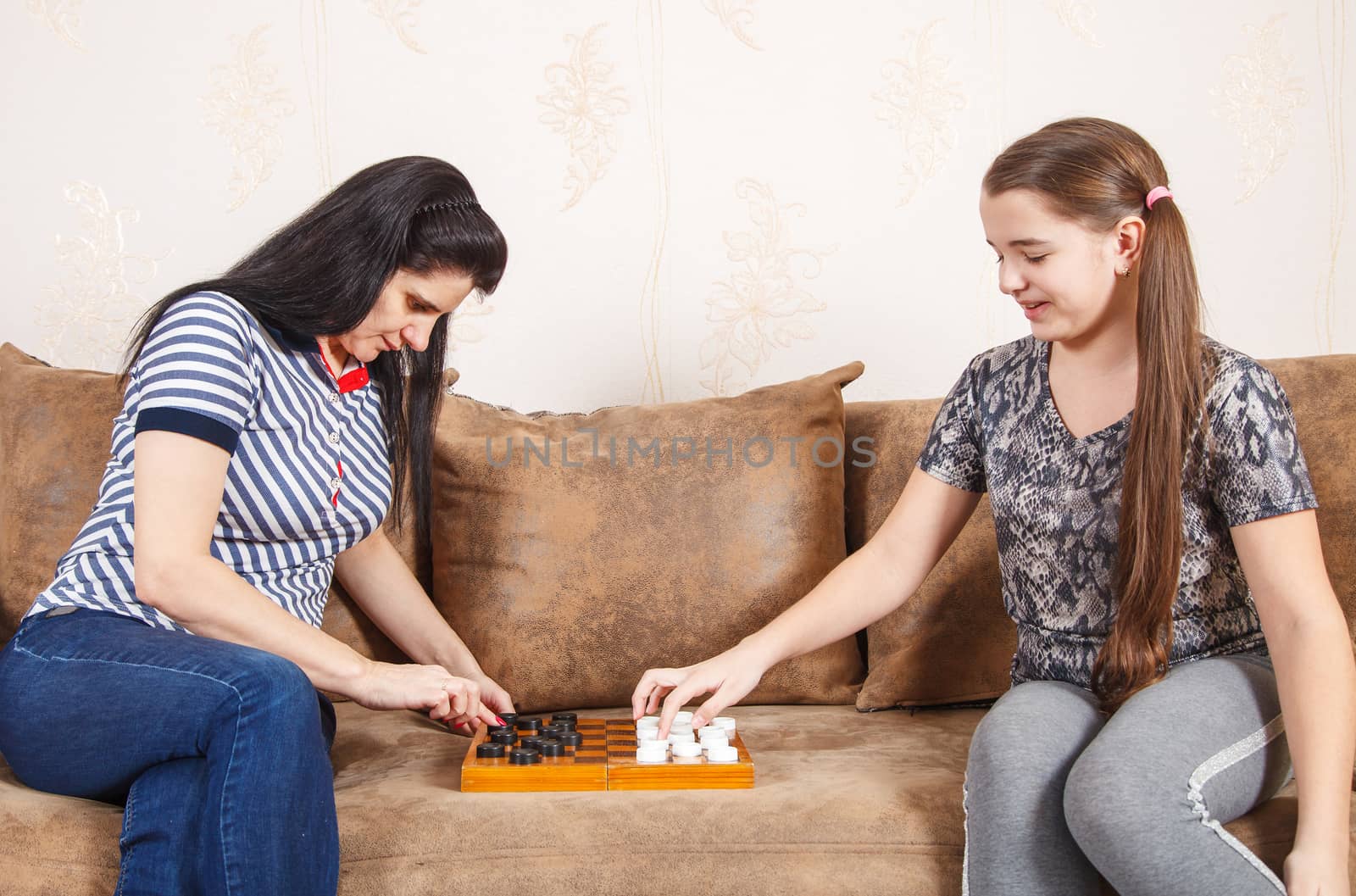 mom and daughter play checkers while sitting on a sofa at home. coronavirus quarantine