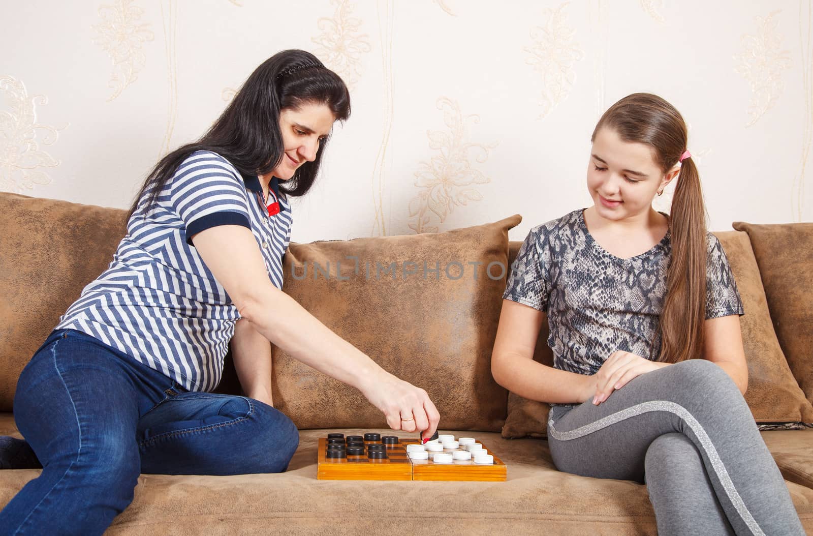mom and daughter play checkers while sitting on a sofa at home. coronavirus quarantine.