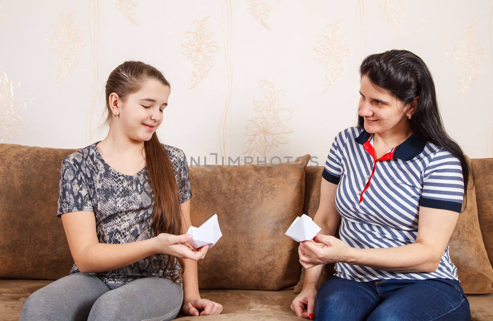 mom and daughter make paper boats while sitting on the sofa at home. coronavirus quarantine