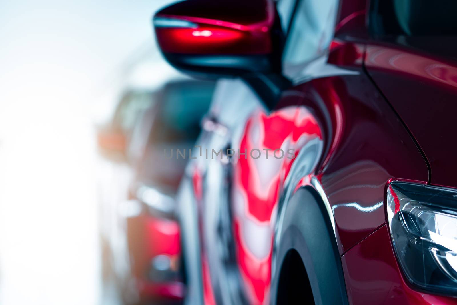 Closeup headlamp of red car parked in modern showroom. New and luxury car. Car dealership concept. Automotive industry. Automobile leasing. Front view of red shiny car parked in a row in showroom.