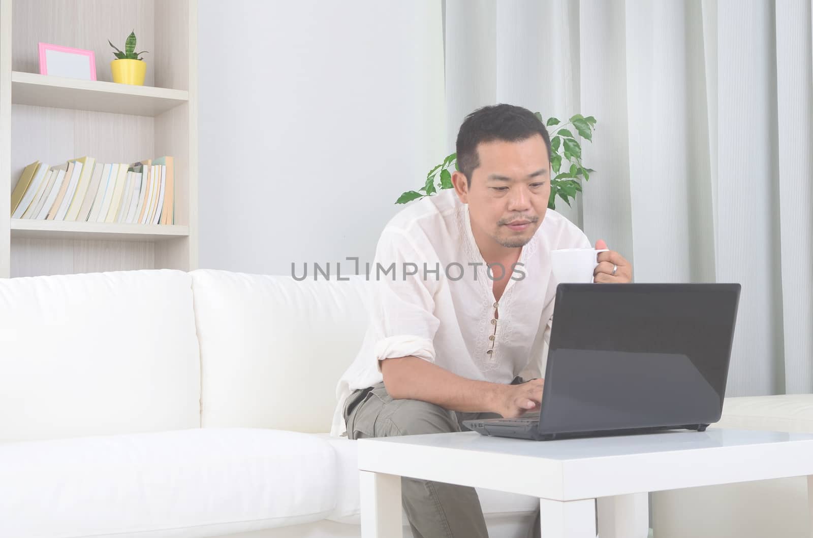 Modern asian man working remotely from home,drinking coffee  during Coronavirus pandemic in the world.