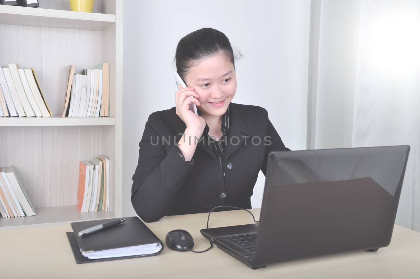 Beautiful Asian young businesswoman working on laptop and talking with  smartphone in the office.