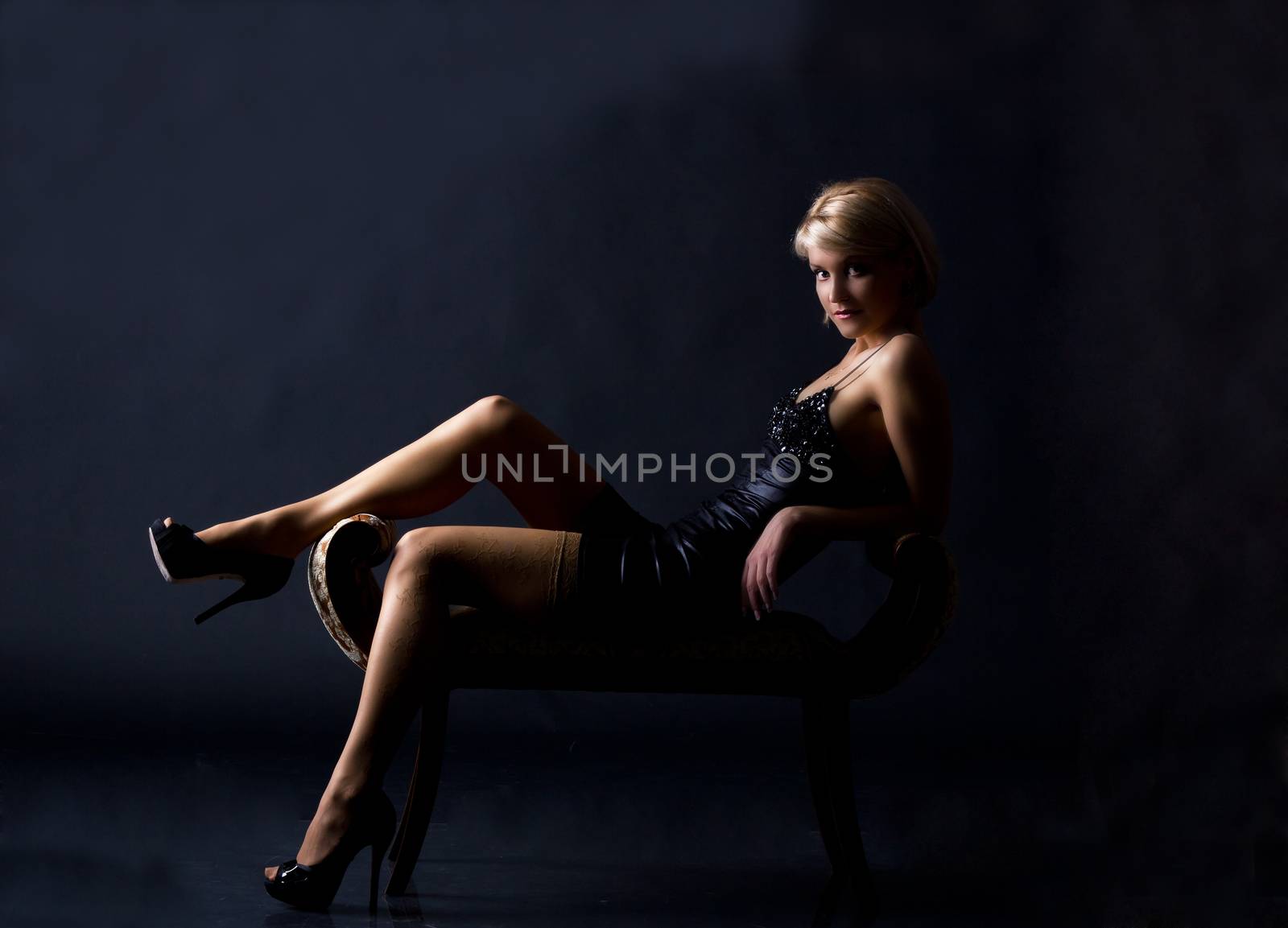 young woman in a black dress posing sitting on dark background