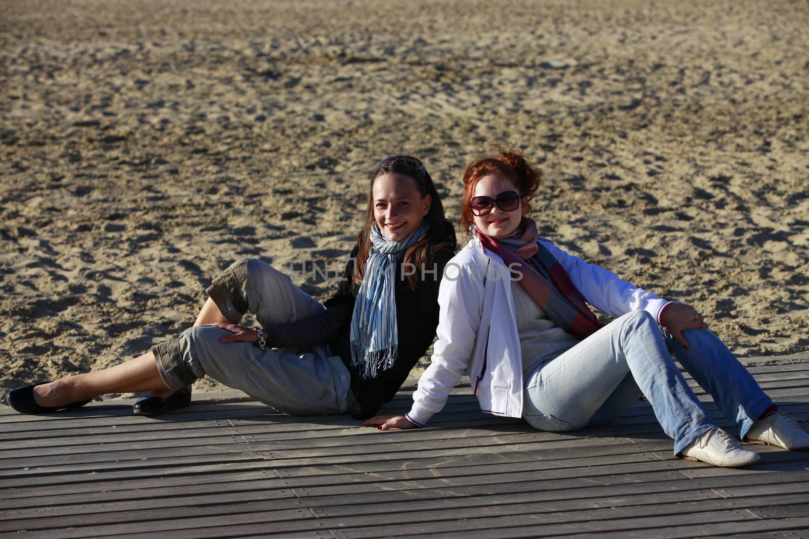 Two girls sits on the wooden bridge at beach