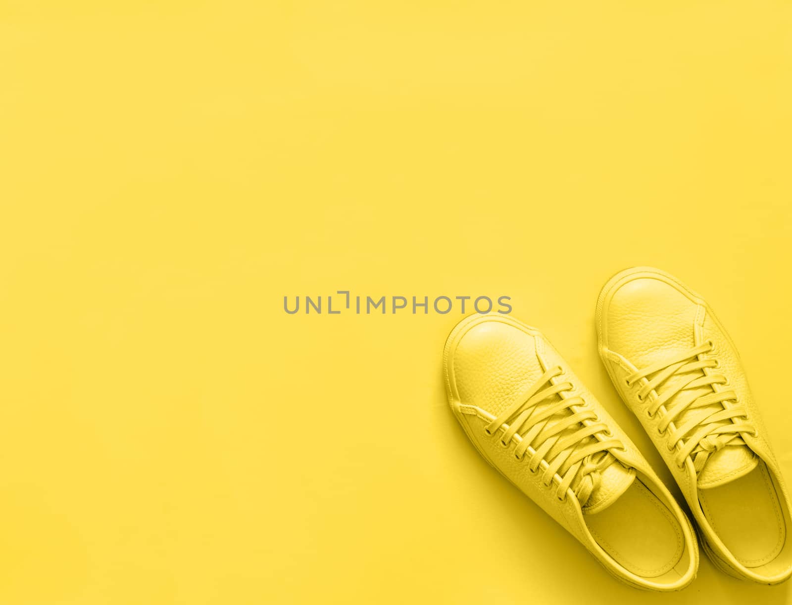 Yellow leather sneakers on yellow background. Pair of yellow sport shoes or sneakers with copy space for text or design. Overhead shot of new yellow sneakers, monochrome. Top view or flat lay