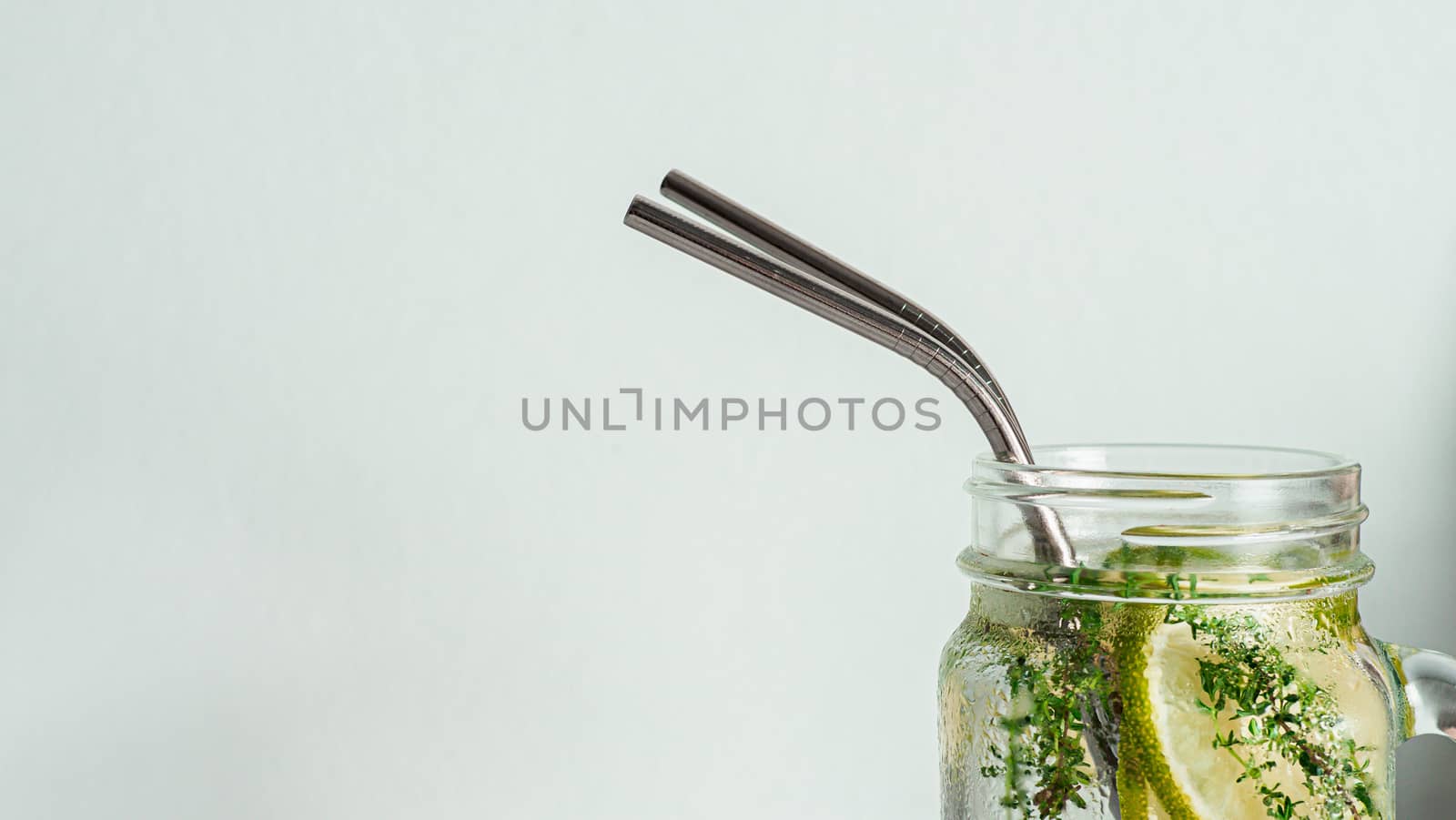 Cold drink in mason jar with metal straw on white background. Lemonade or detox water with lime and thyme in glass jar with copy space for text or design. Recyclable straws, zero waste concept. Banner