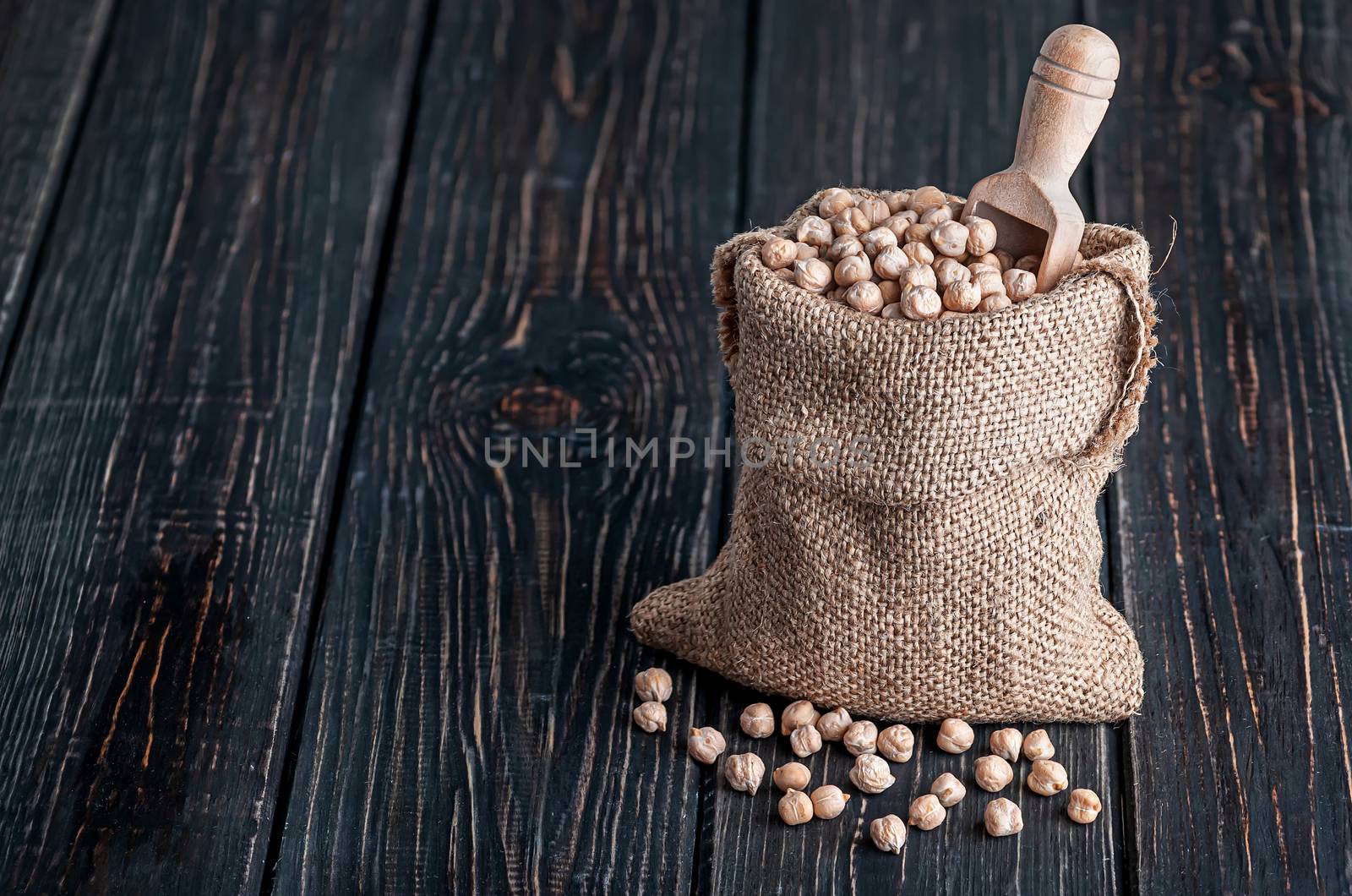 Sack with chickpeas and spoon stands on wooden background