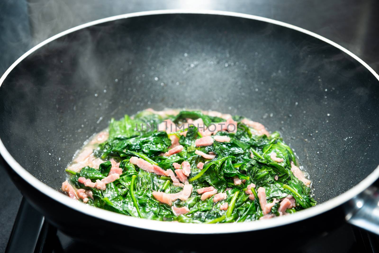 Cooking spinach with diced bacon in nonstick wok