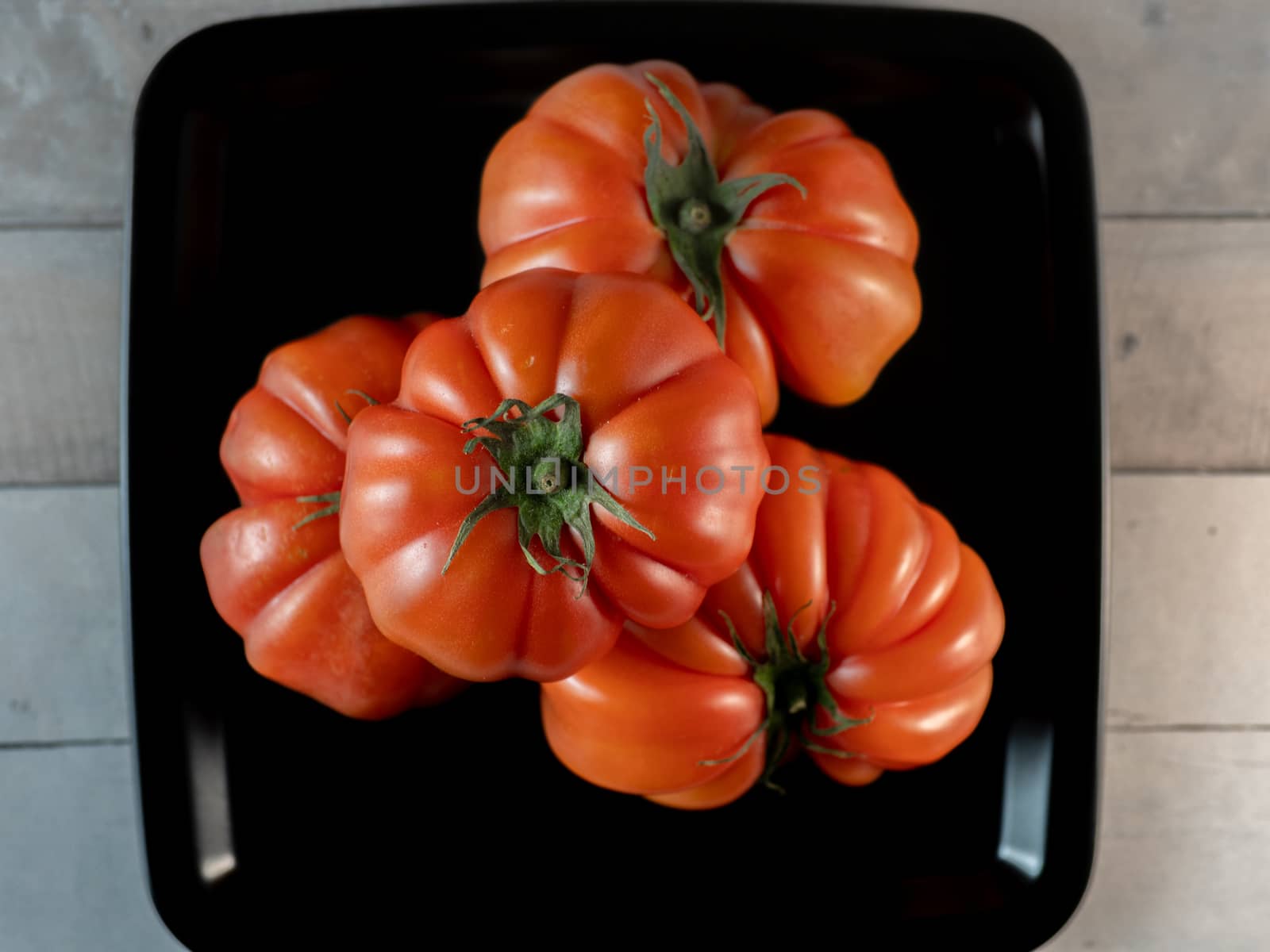 tomatoes in black plate on light table by jmagfoto