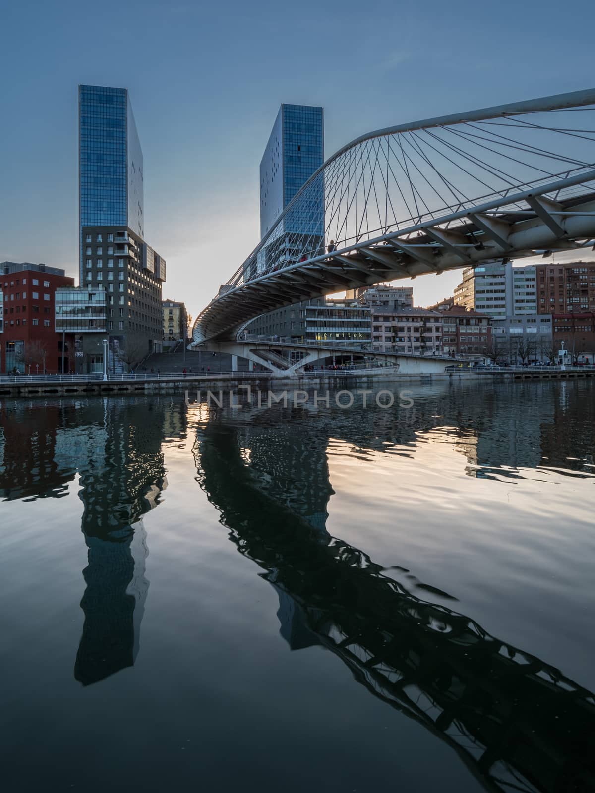 twin skyscrapers with white bridge spanning a river by jmagfoto