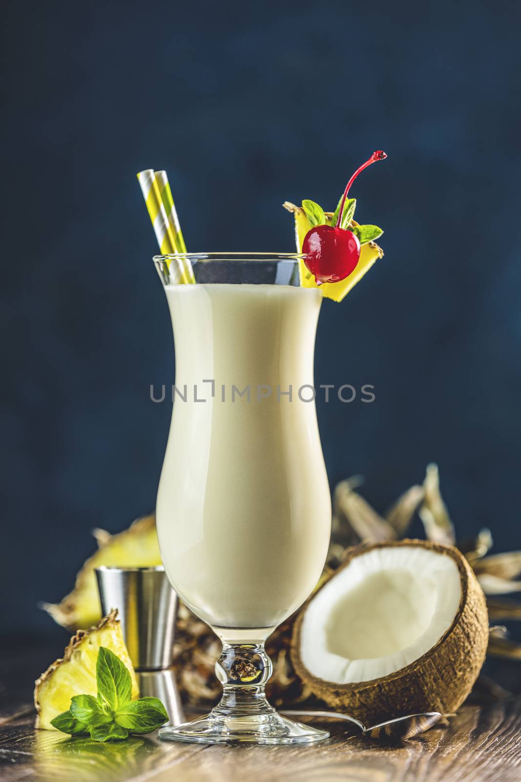 Glass of tasty Frozen Pina Colada Traditional Caribbean cocktail decorated by slice of pineapple and cherry, served on dark wooden background.