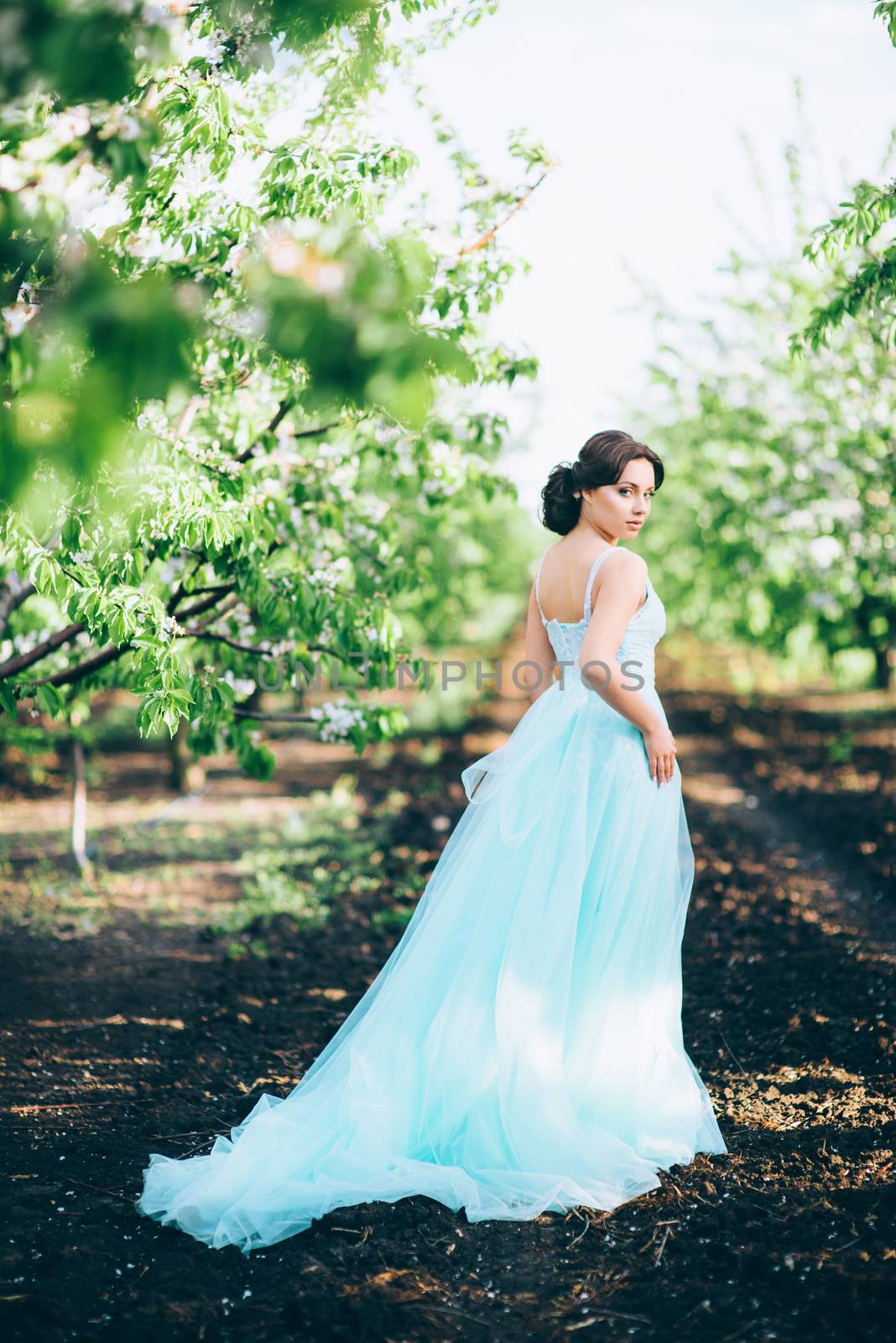 brunette girl in a turquoise dress walking in the spring garden