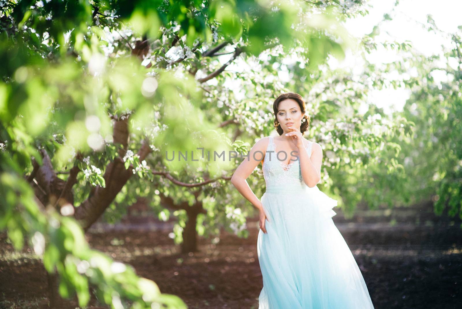 brunette girl in a turquoise dress walking in the spring garden