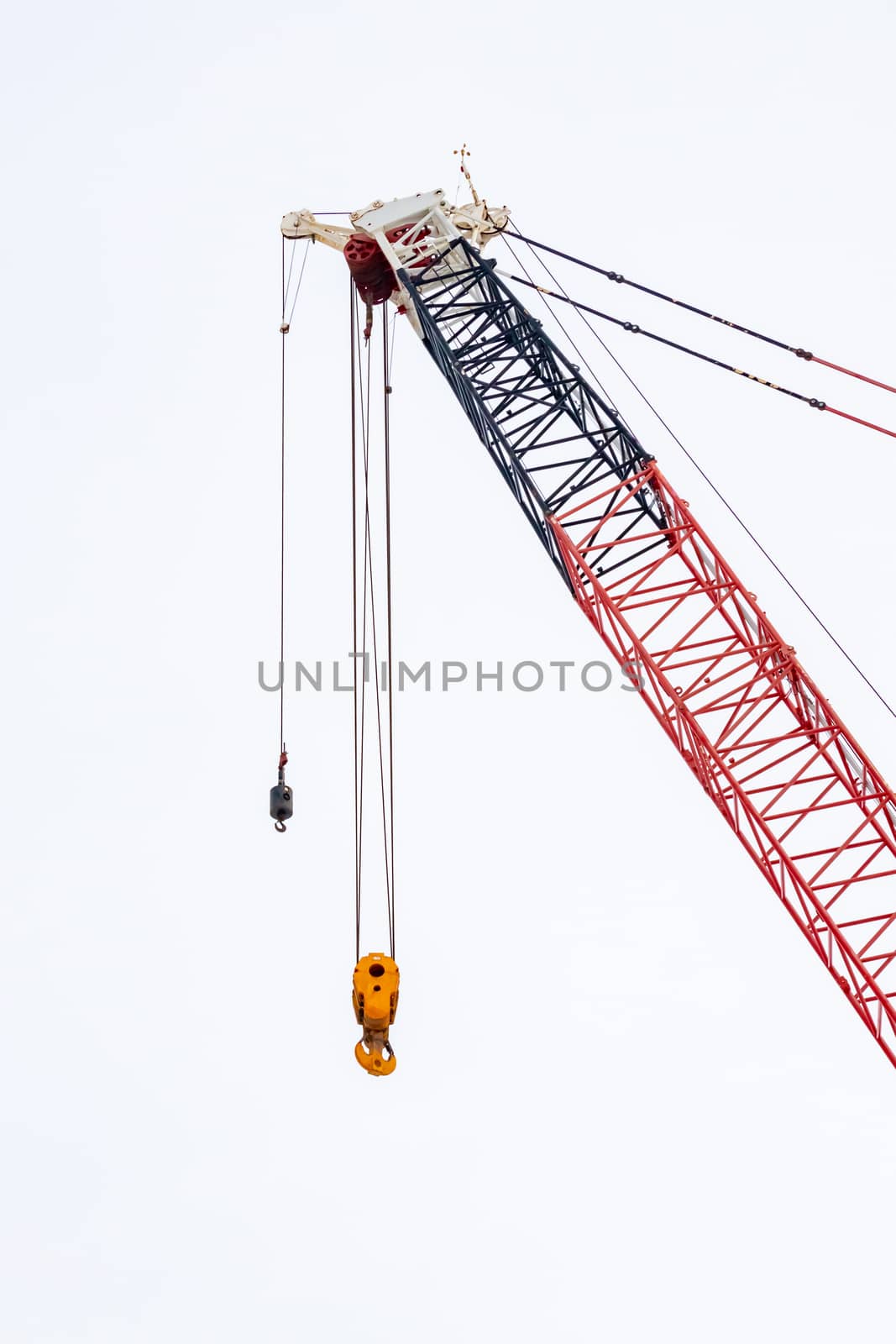 A construction crane has hanging metal pulleys and hooks and does not currently carry anything.