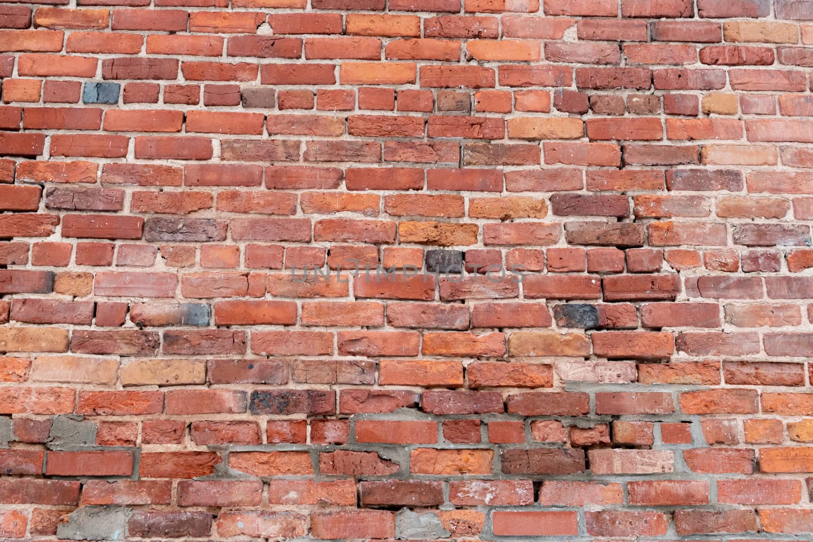 An old wall of red bricks with several parts of the masonry showing their age, damage and replacement by mismatched bricks creates a unique texture and pattern.