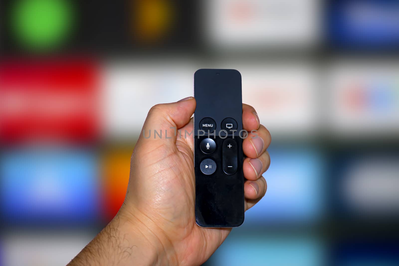 A person holding a digital media player and microconsole remote with a television screen on the background