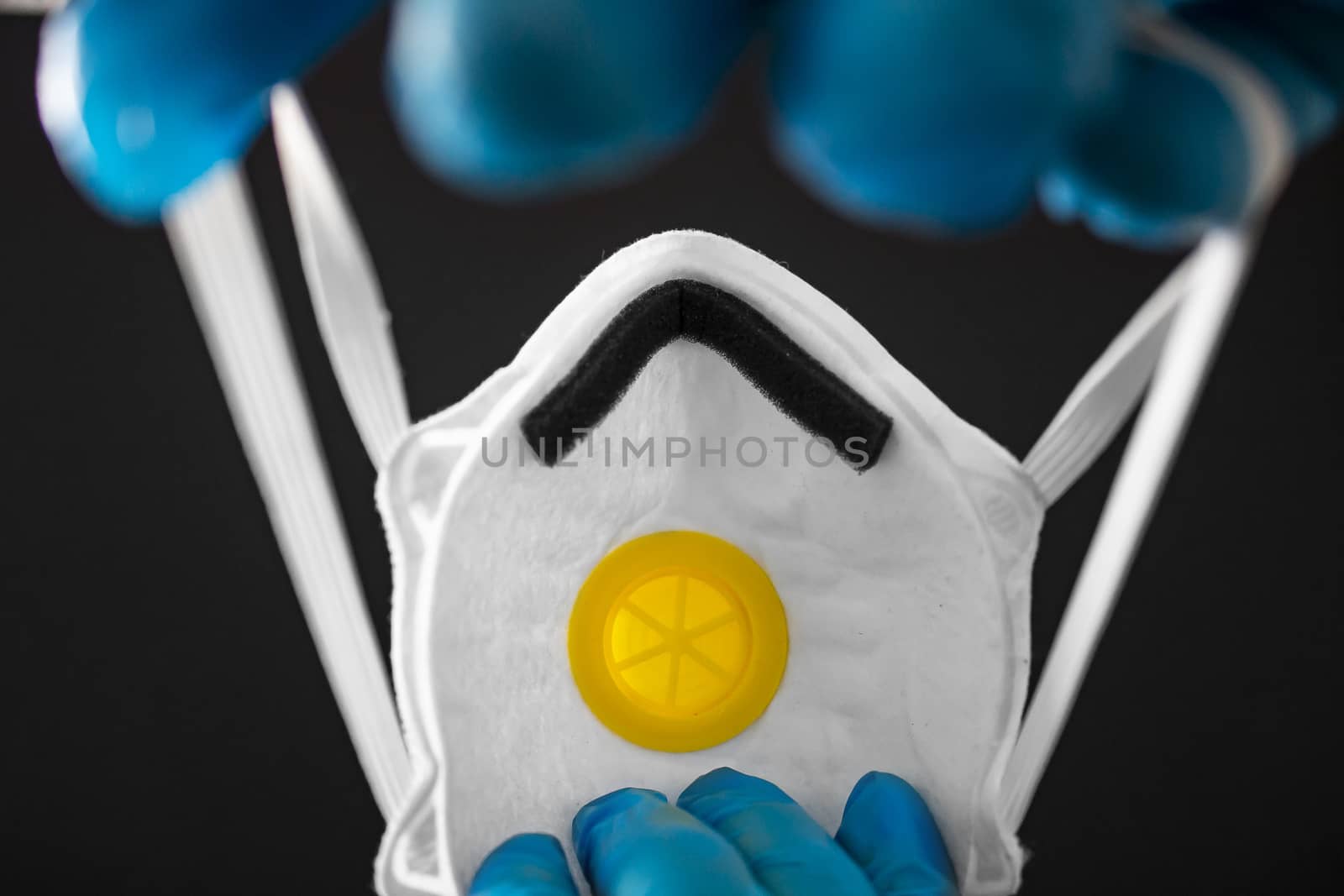 A person wearing medical gloves about to wear a N95 face mask on a black backgound