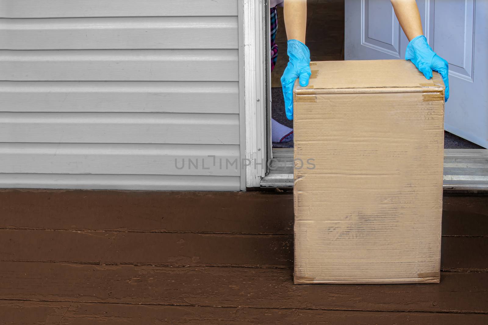 A person wearing gloves, picking up a deliver box from a home entrance