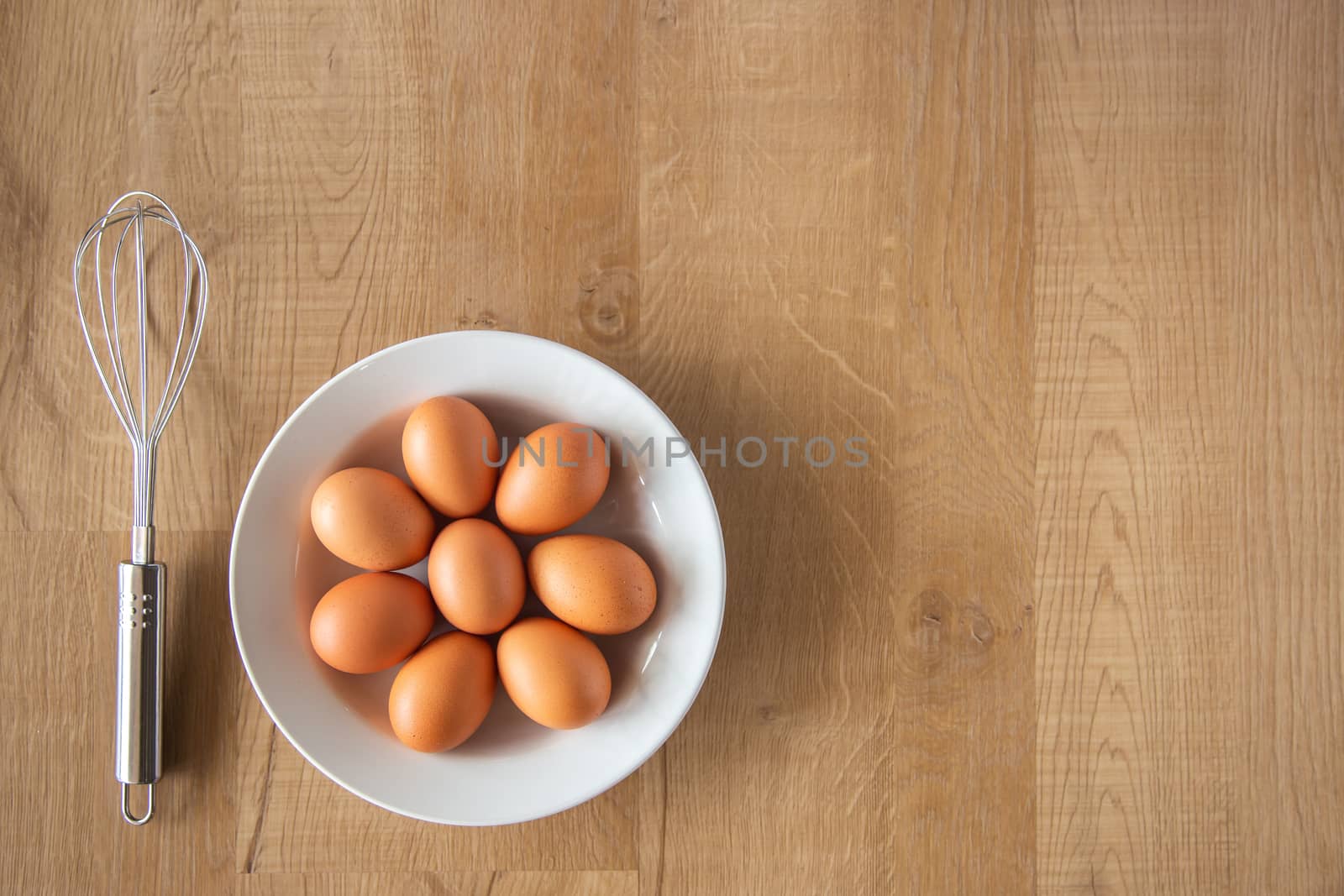 Chicken eggs and egg beater on wooden background.