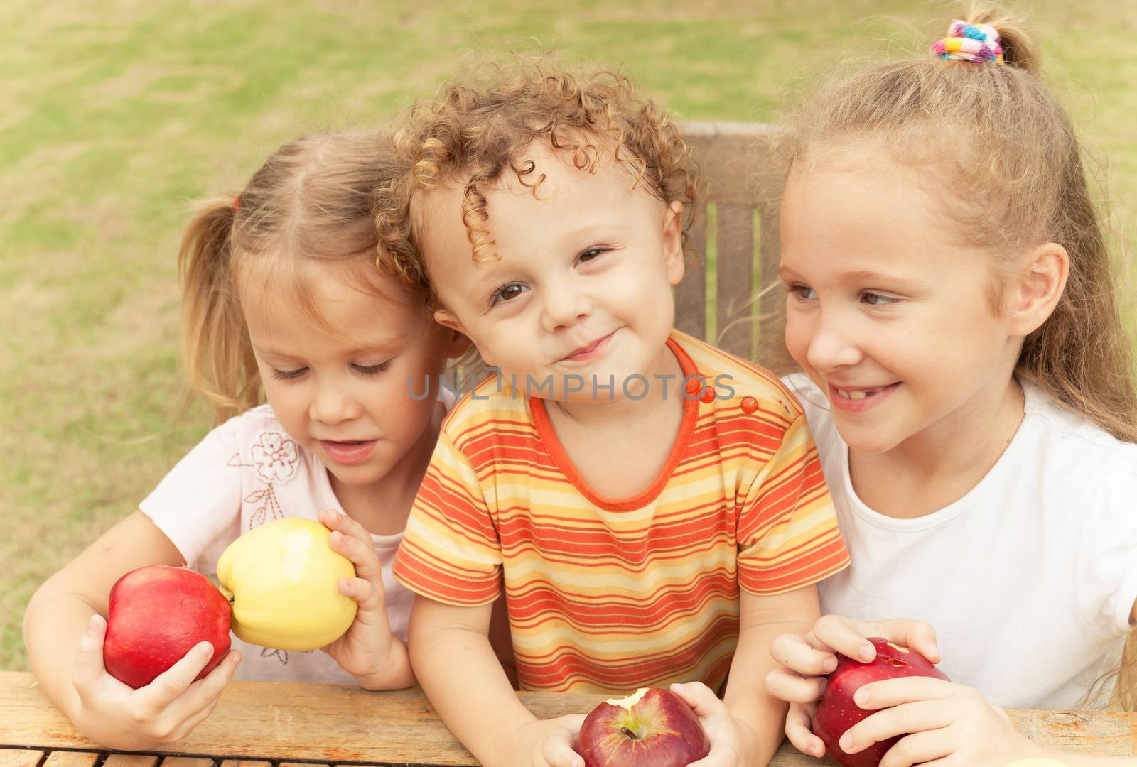 three happy children sitting at the table and eat apples