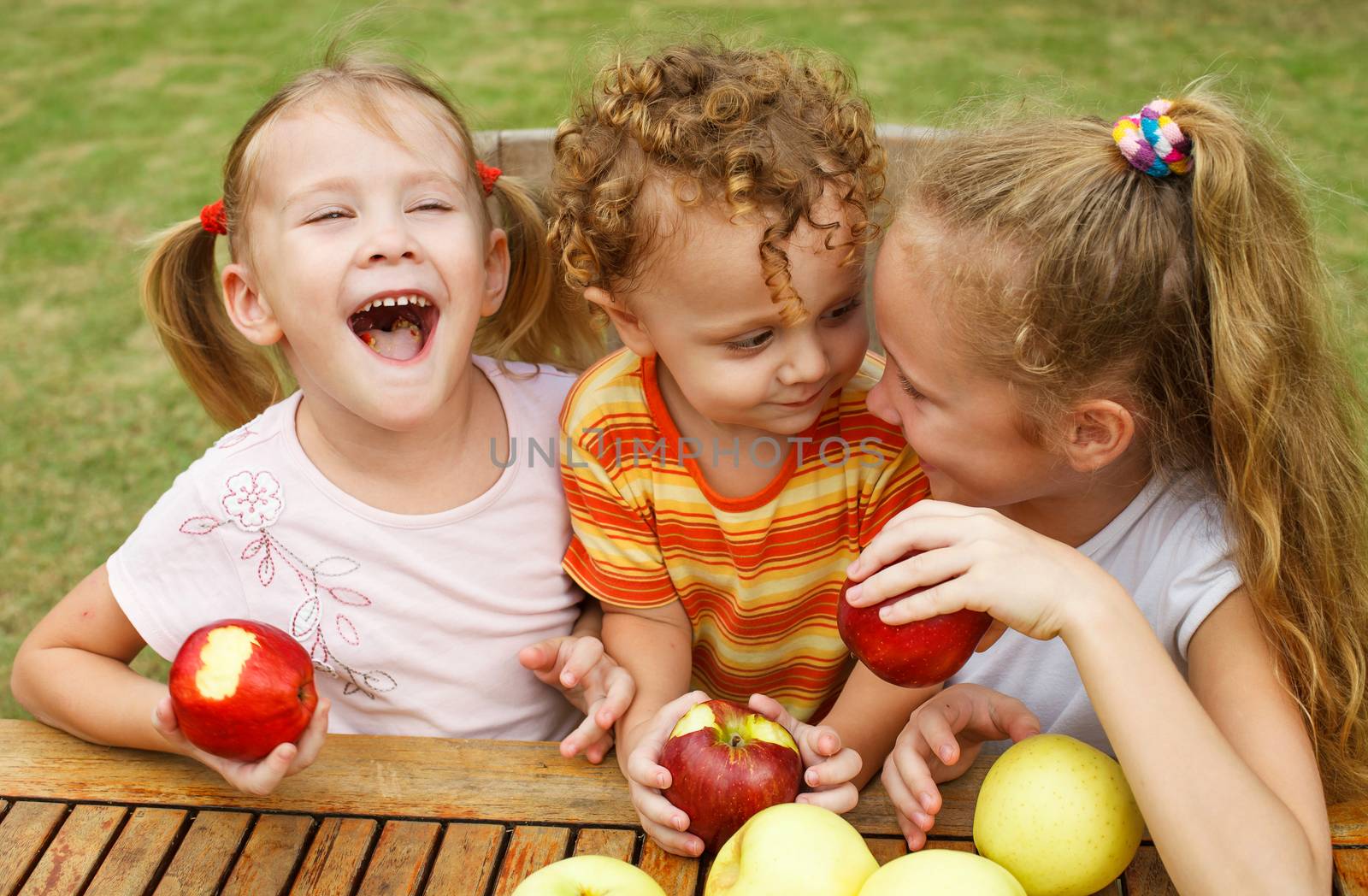 three happy children sitting at the table and eat apples