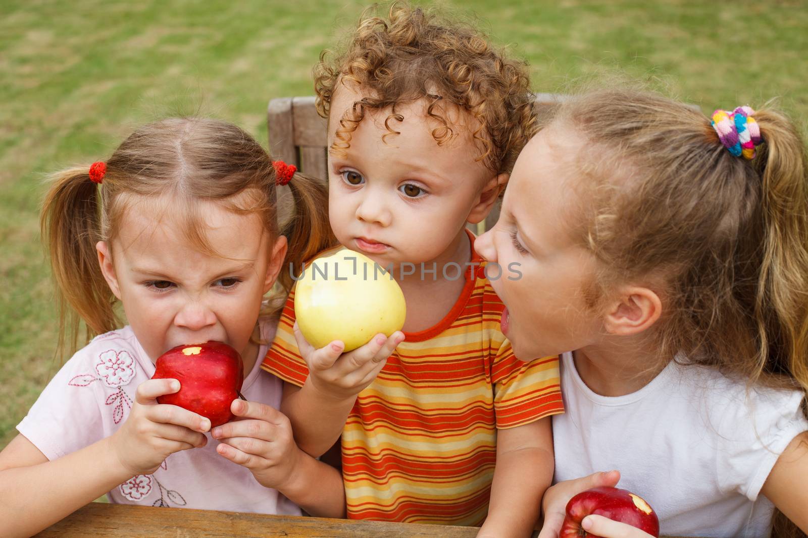 three happy children sitting at the table and eat apples