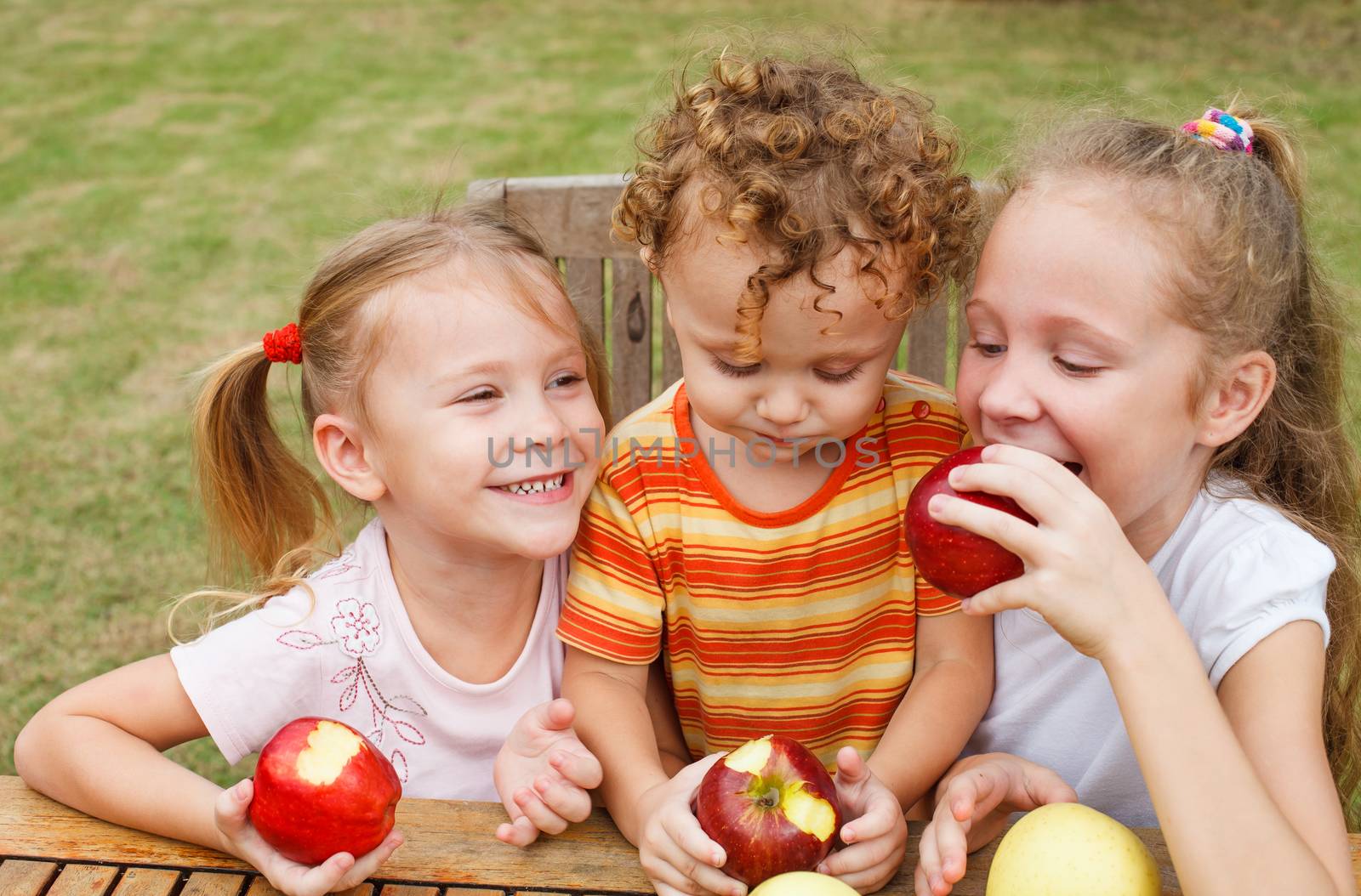 three happy children sitting at the table and eat apples