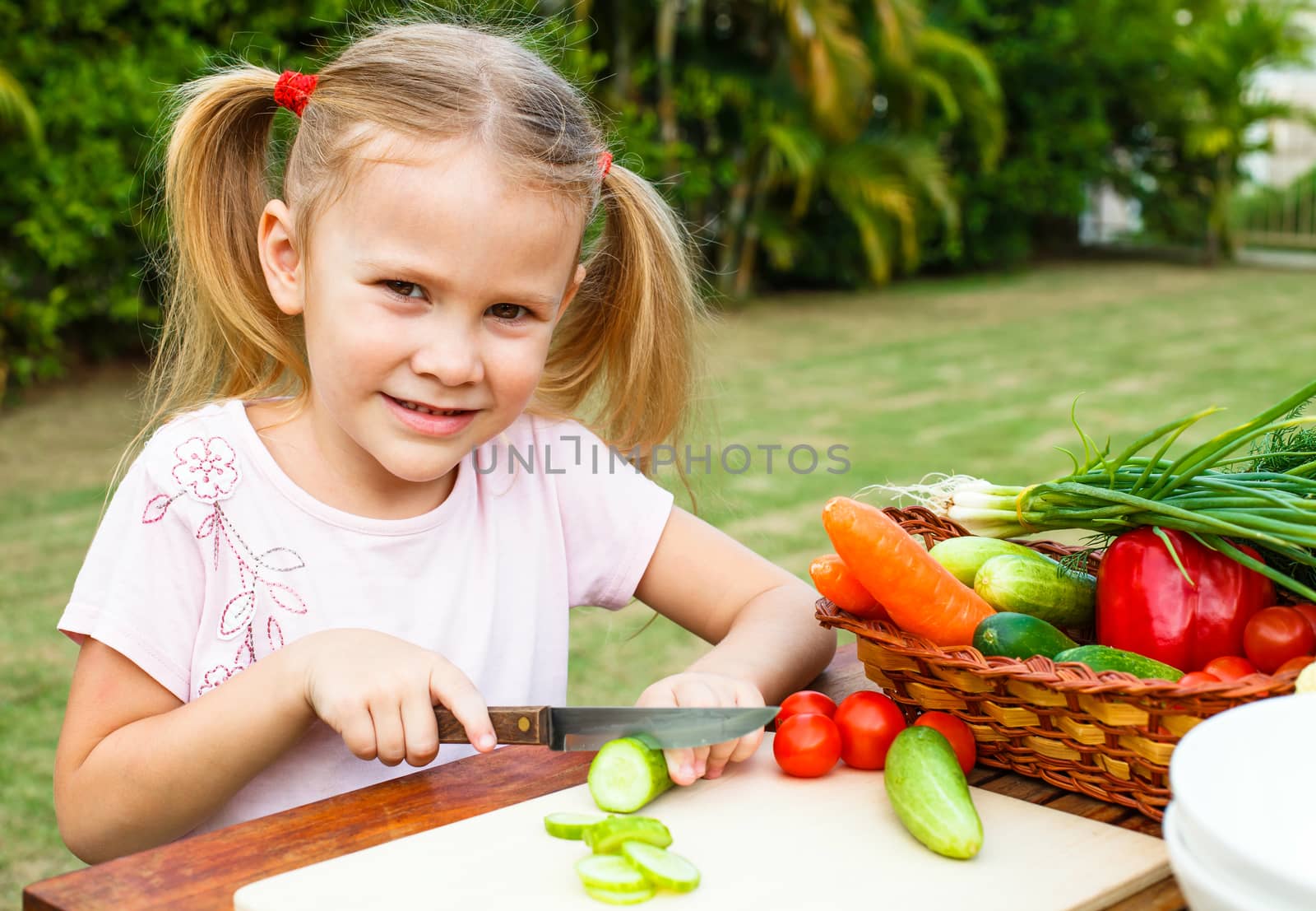 Little girl cutting vegetable for salad. Concept of healthy food.