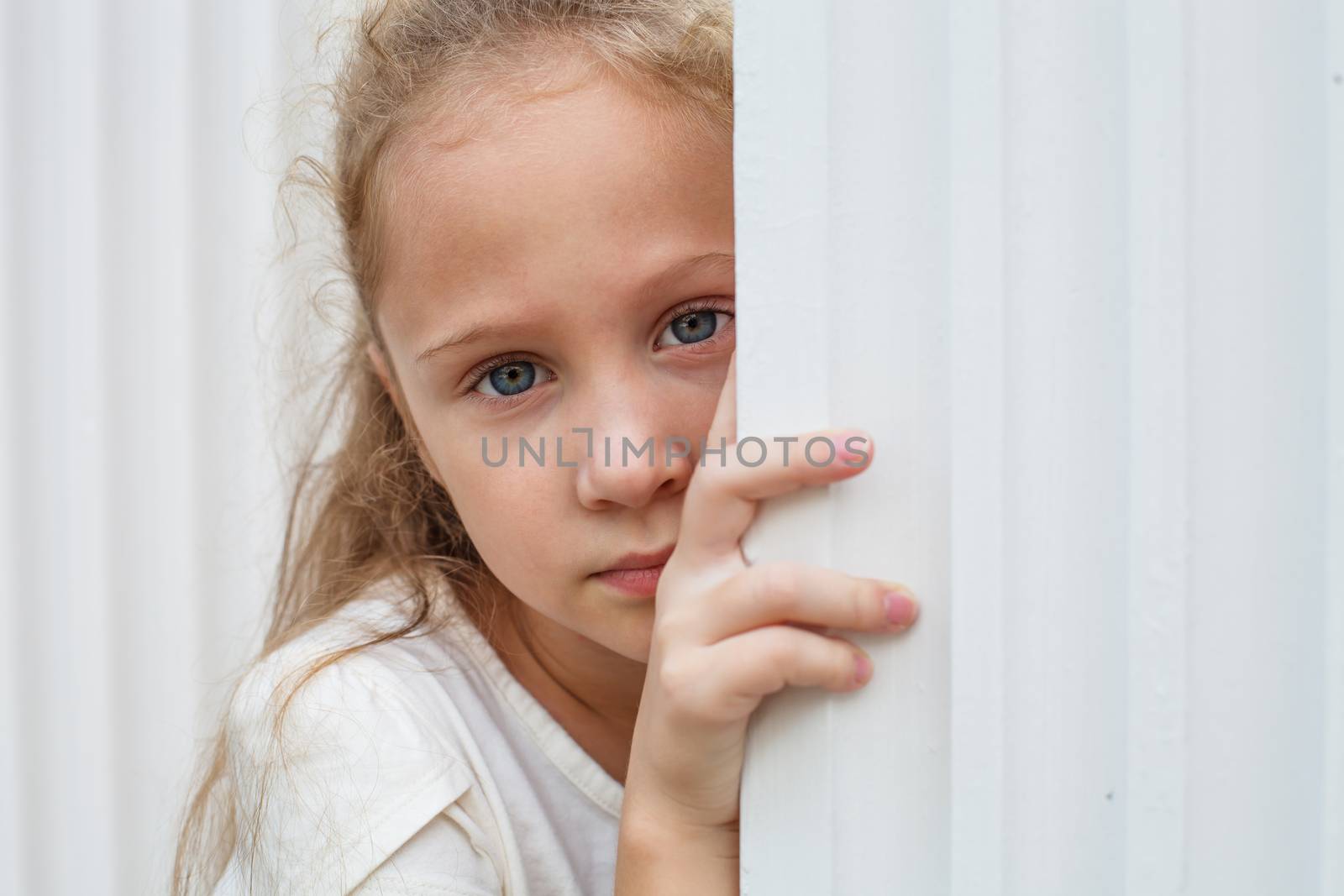 Sad little girl near the white wall.