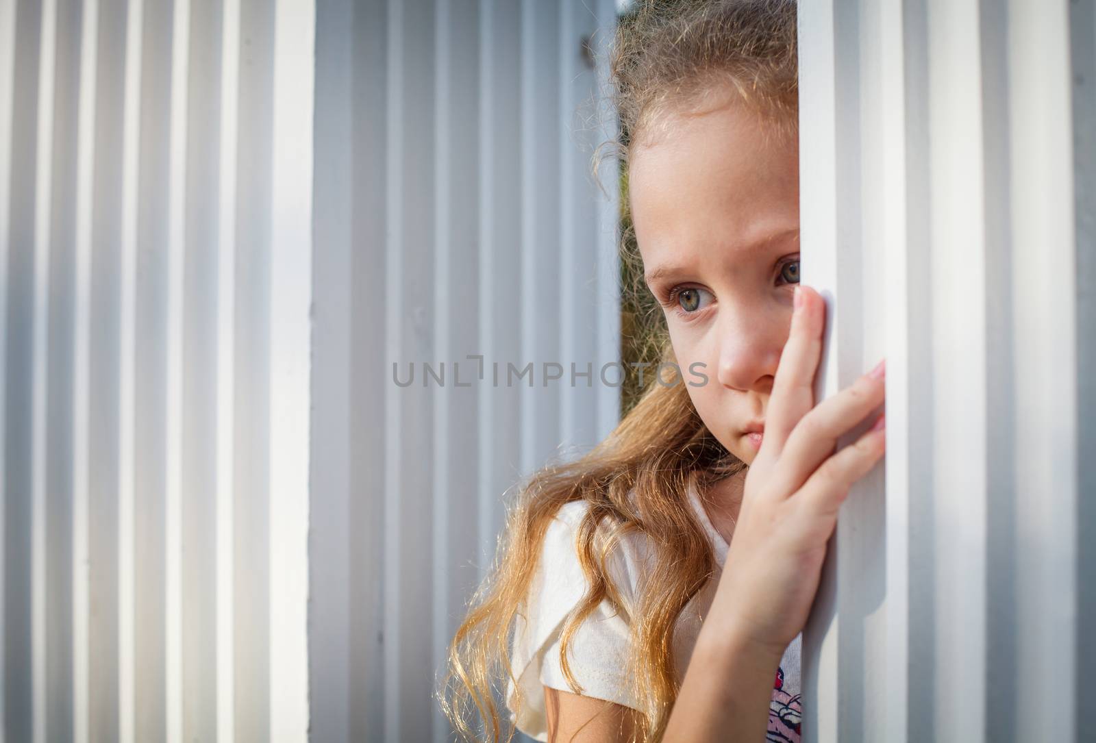 Sad little girl near the white wall.