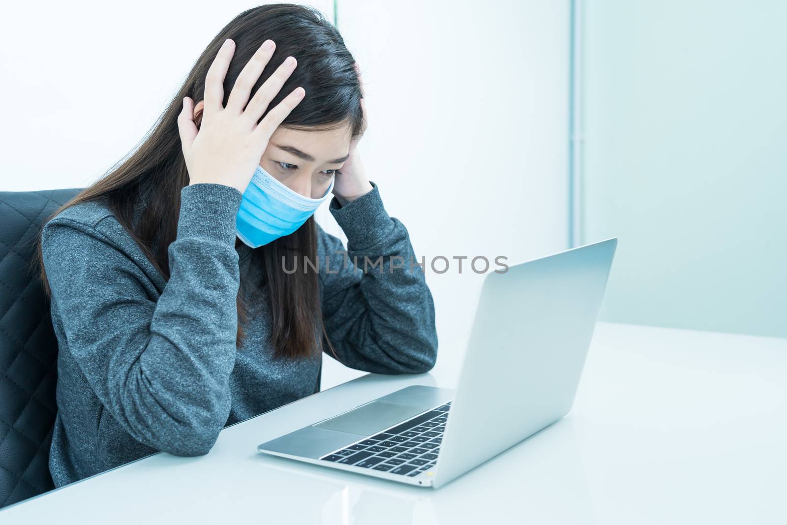 Woman using a laptop on the desk with headache and wearing  protective mask for protection against virus Covid-19