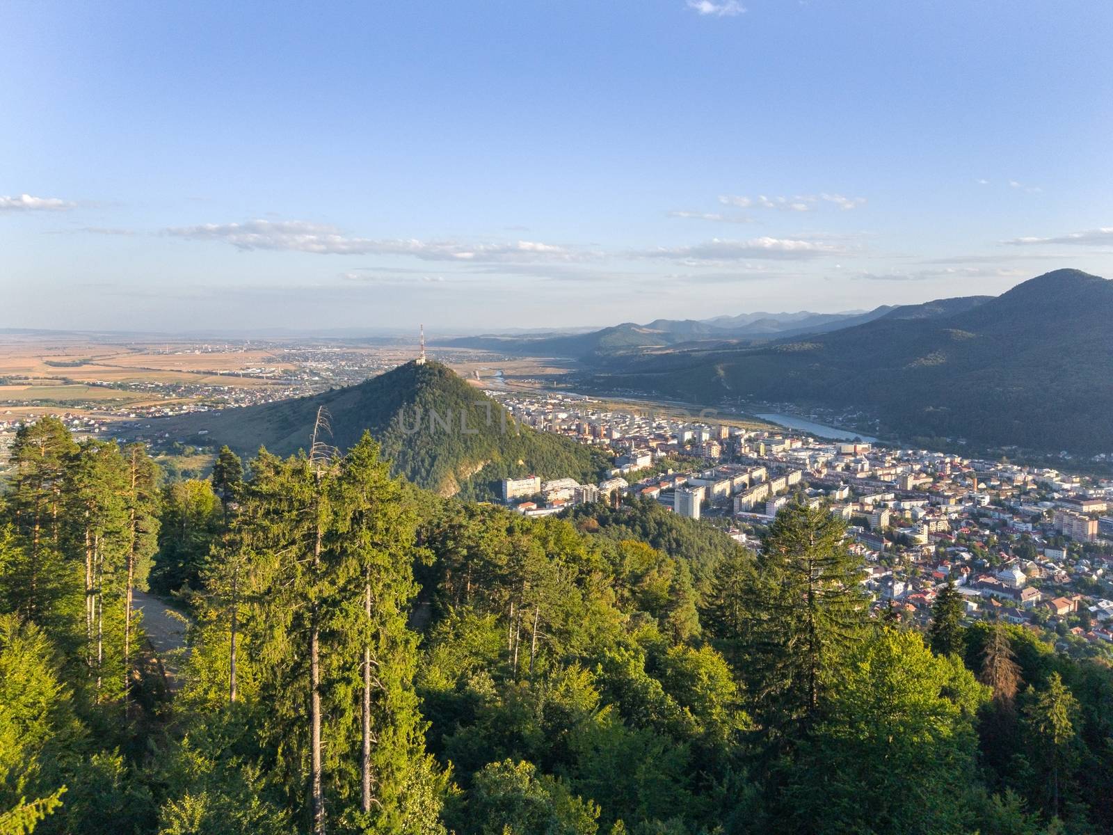 The forest and the city in the valley at sunset. Aerial view in Romania, Piatra Neamt.