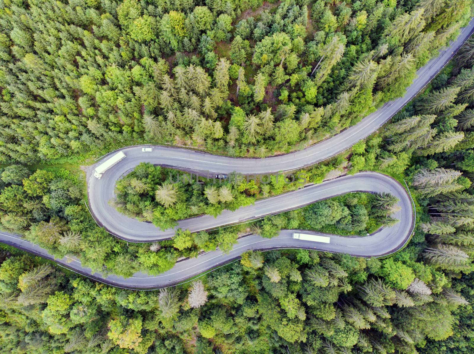 Above view of winding mountain pass road through green forest, Romania