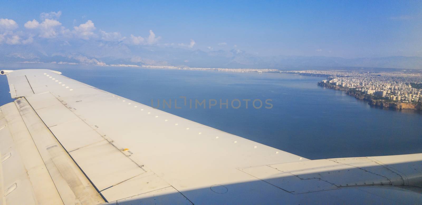 Plane flying over the sea prepairing for land to Antalya, Turkey. Rocky coast of the Mediterranean Sea and modern buildings in the city