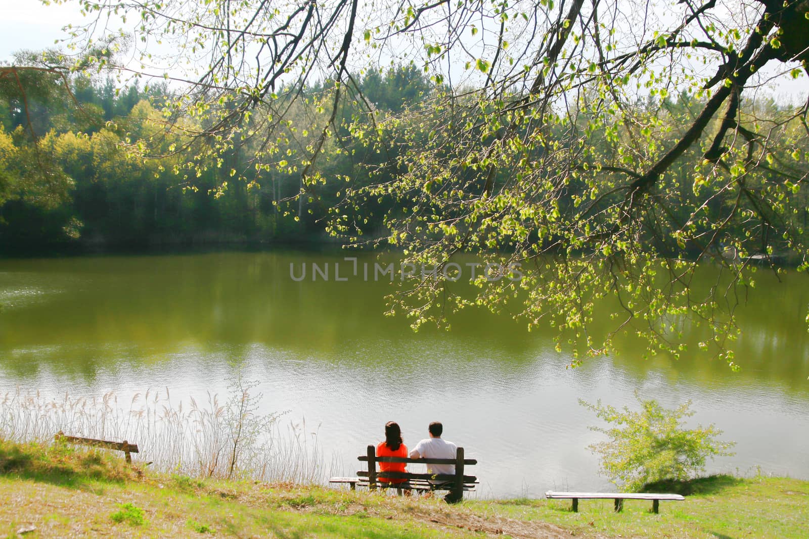 Two people on bench near the lake. Lake, mountain and sunlight