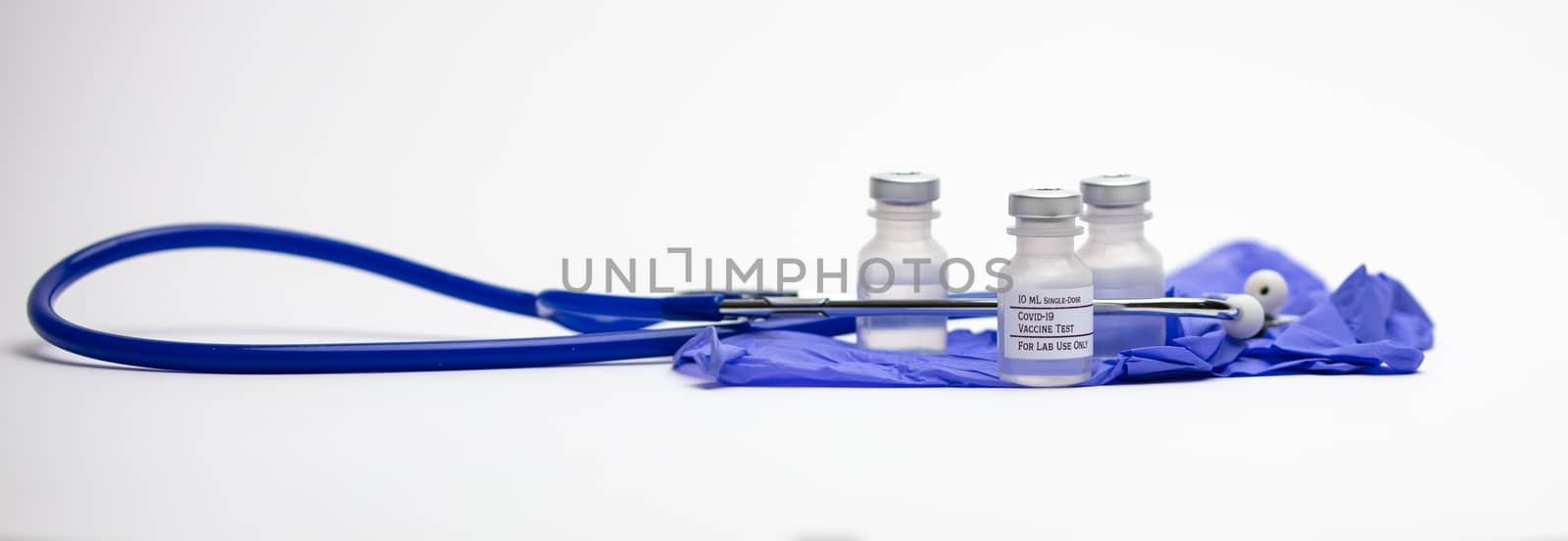 Three Covid-19 test vaccine vials on top of blue medical gloves and surrounded by a blue stethoscope.