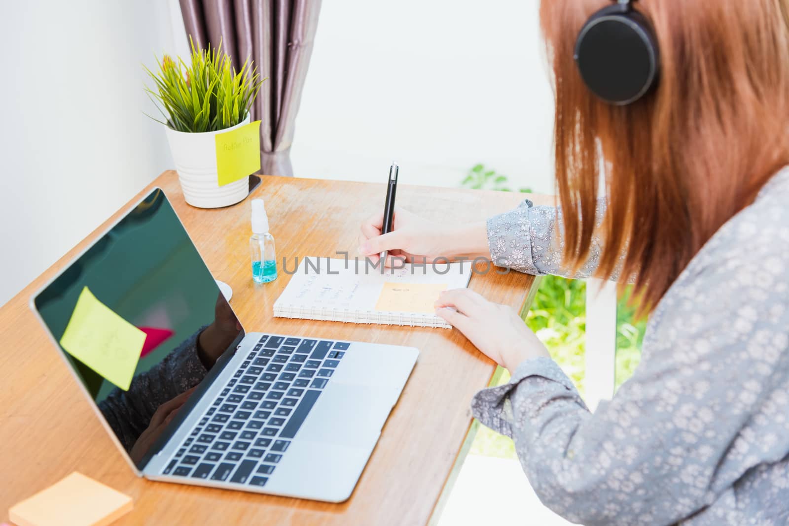 Asian young business woman wearing face mask protective working from home office with laptop computer he quarantines disease coronavirus or COVID-19 and write note booklist work today
