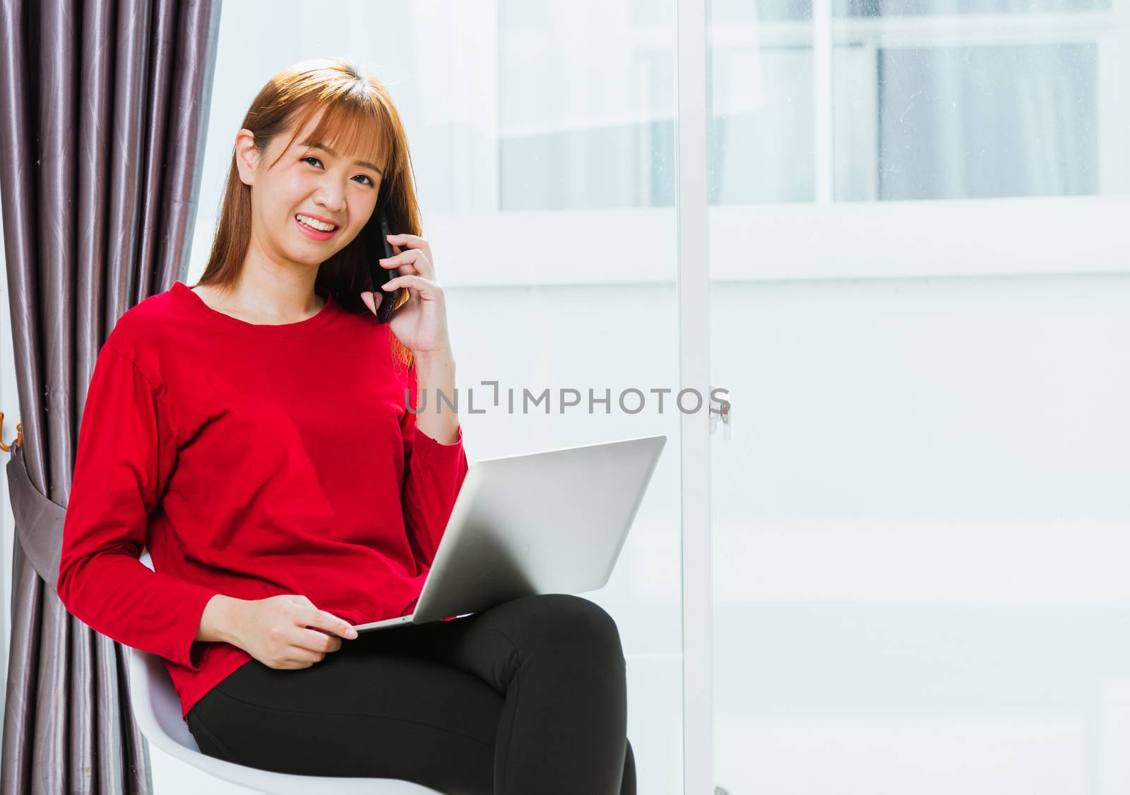 Work from home concept, Asian beautiful young woman smiling, student girl sitting on chair using mobile phone call director to team during working with laptop computer at home office