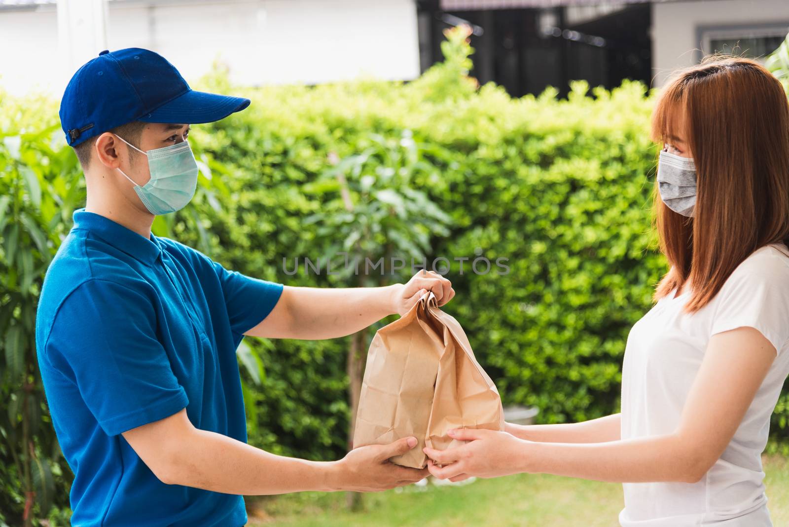 Asian delivery express courier young man giving paper bags fast food to woman customer receiving both protective face mask, under curfew quarantine pandemic coronavirus COVID-19