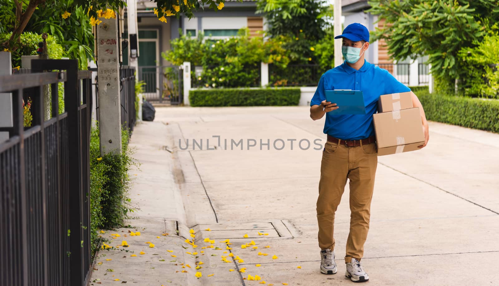 Asian young delivery man courier hold parcel post boxes he protective face mask service and walk looking for customer home location, under curfew pandemic coronavirus COVID-19