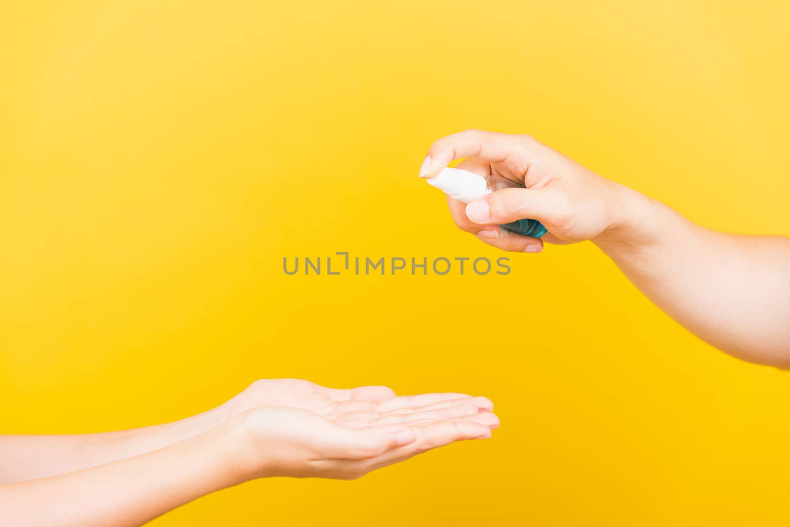 Family man applying hand spraying blue alcohol spray sanitizer clean and disinfect woman hands, Protection Covid-19 coronavirus outbreak, studio shot isolated on yellow background