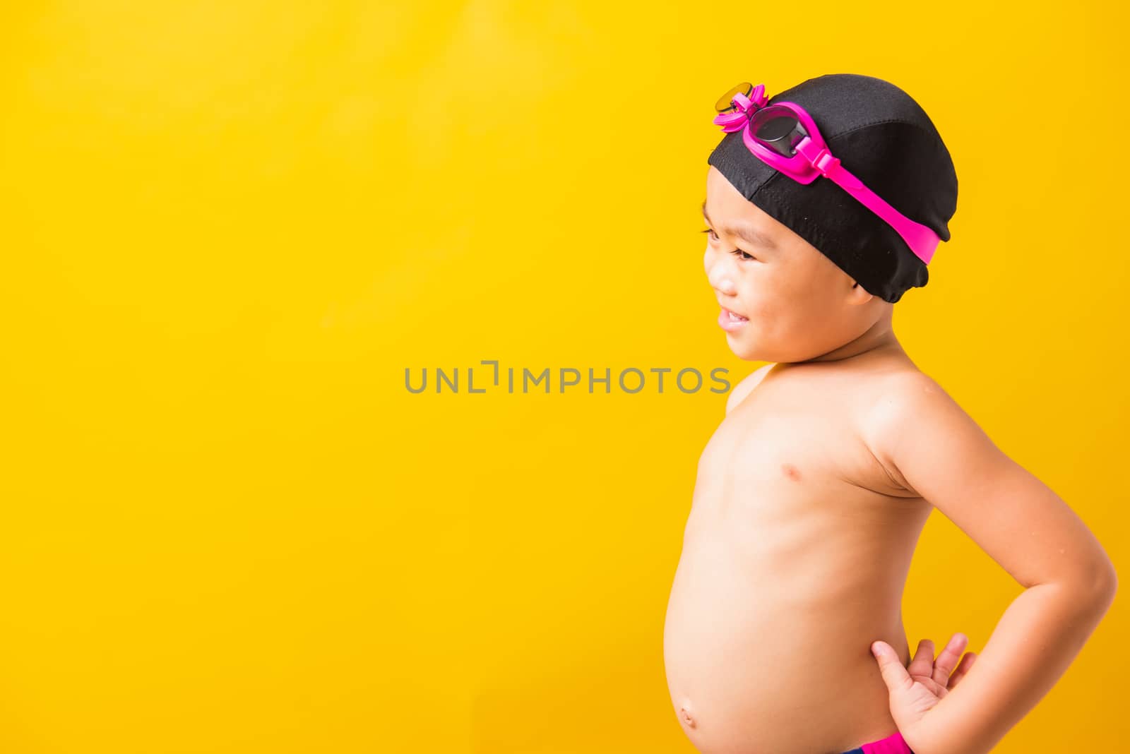 Summer vacation concept, Closeup portrait Asian happy cute little child boy wearing goggles and swimsuit, Kid having fun with in summer vacation looking side, studio shot isolated yellow background
