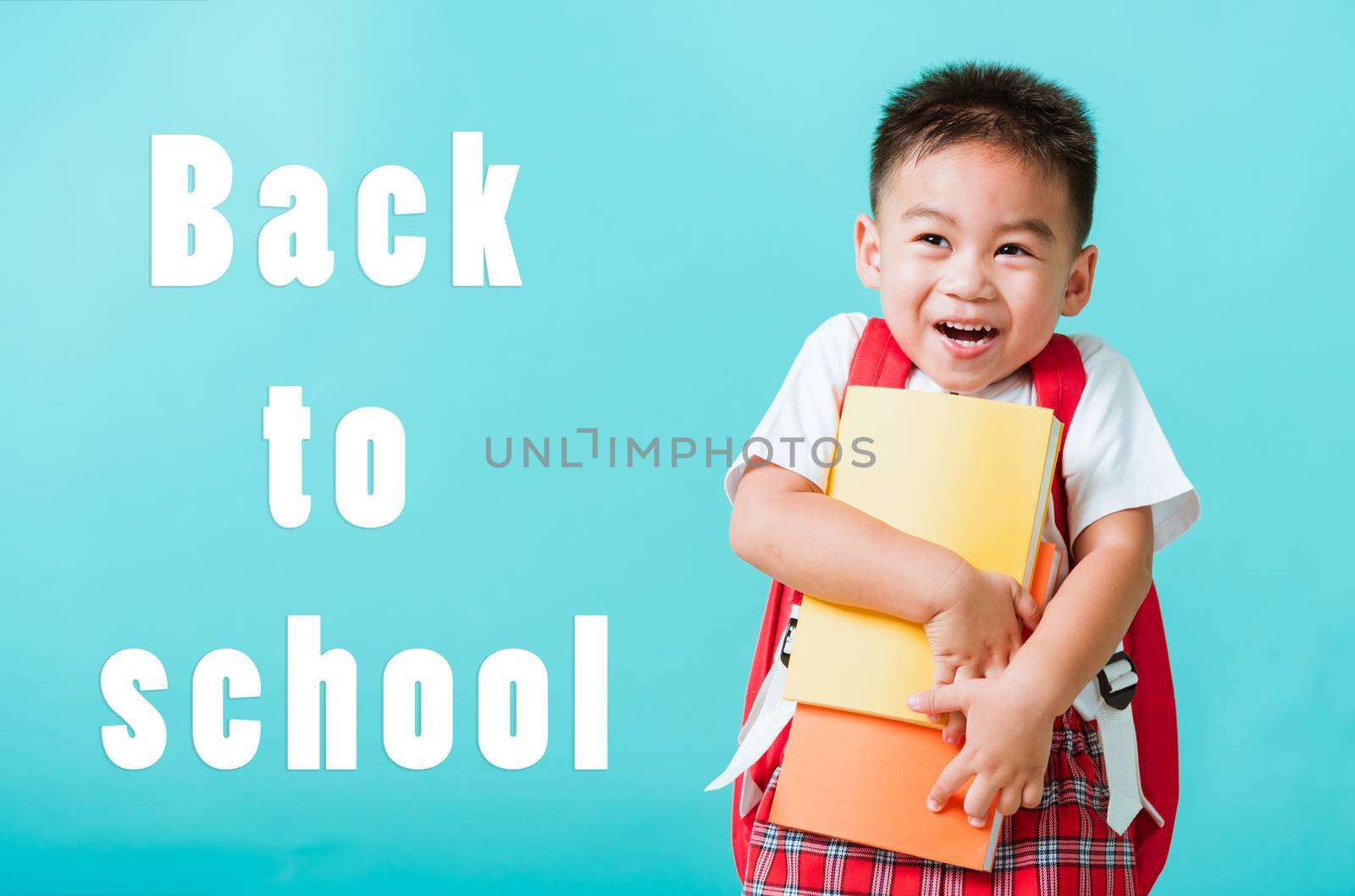 Back to school concept. Portrait Asian happy funny cute little child boy smiling and laugh hug books, studio shot isolated blue background. Kid from preschool kindergarten with school bag education