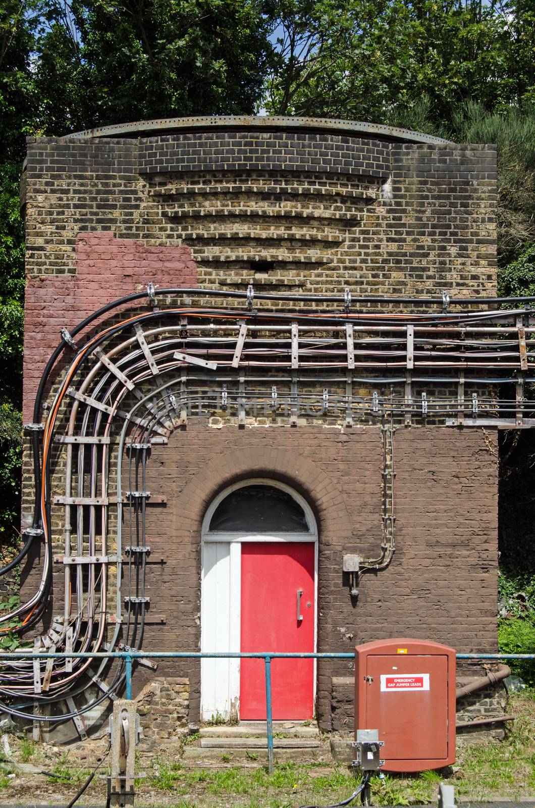 A small brick Art Deco building covered in electrical cables in the sidings at Ealing Broadway station in West London.